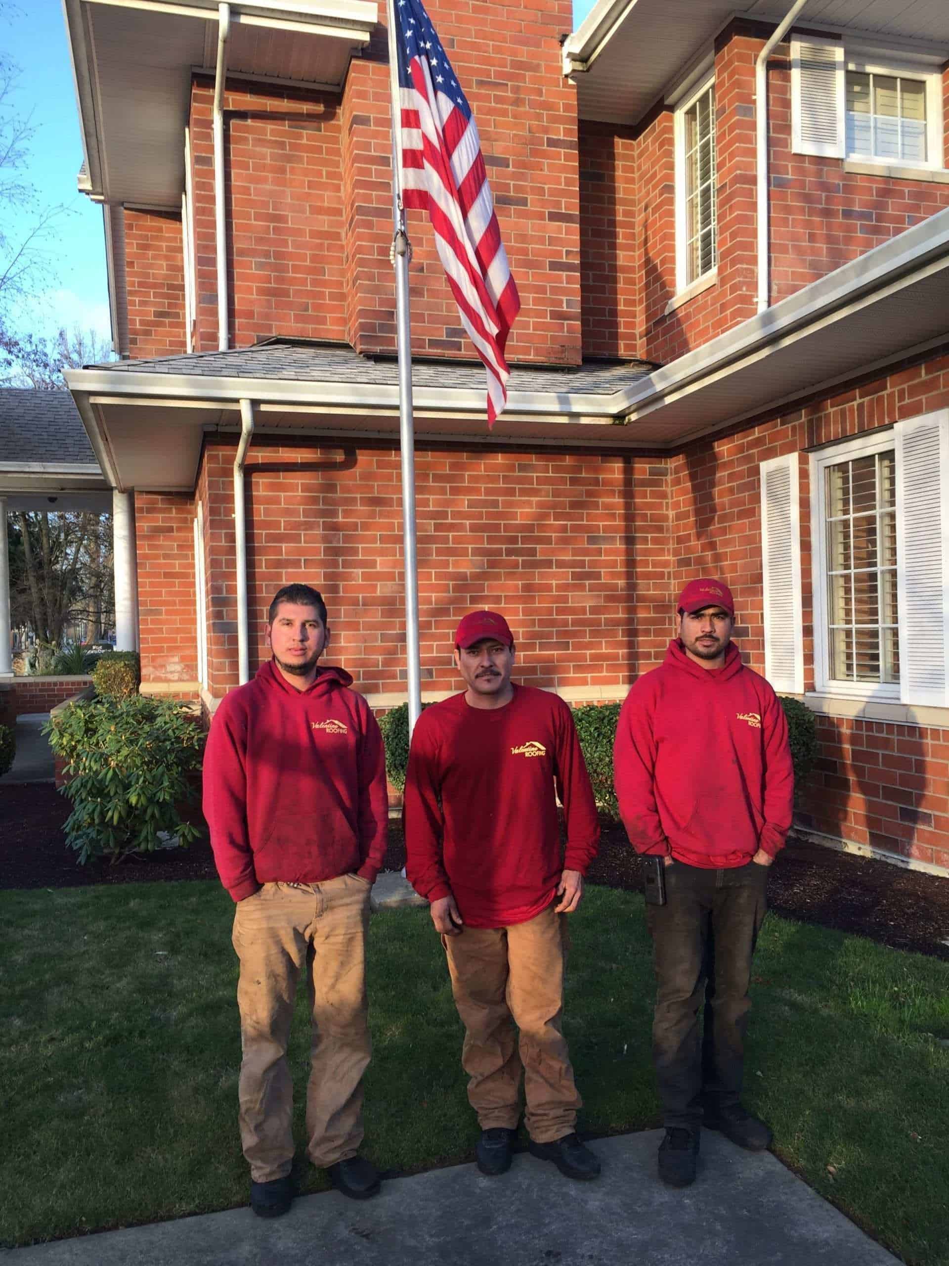 3 male roofers standing under a flag of the United States