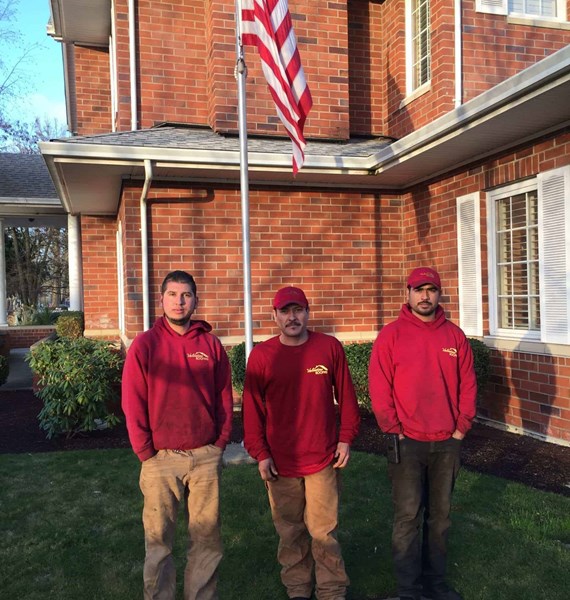 3 male roofers standing under a flag of the United States