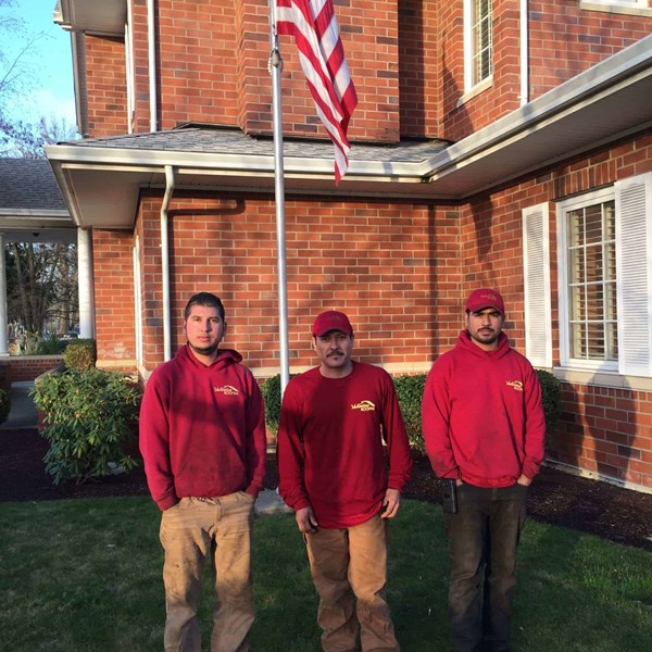 3 male roofers standing under a flag of the United States