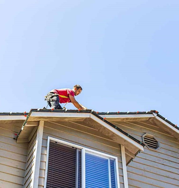 Worker installing Christmas lights on a roof in Seattle, WA