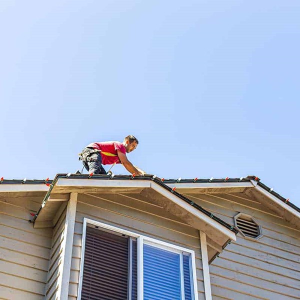 Worker installing Christmas lights on a roof in Seattle, WA